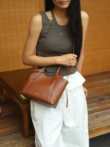 Detailed shot of brown leather shoulder bag, vintage tote design with metal hardware in scene.