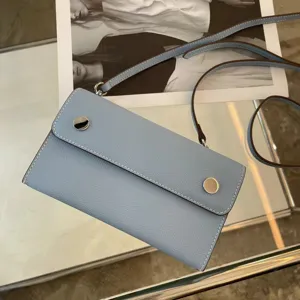 Detailaufnahme einer hellblauen Leder Umhängetasche mit feiner Textur und Metall-Druckknopf.