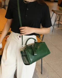 Close-up detail shot of a vintage dark green leather boston bag worn by a model indoors.