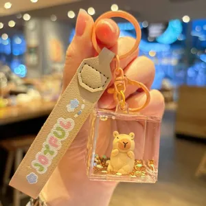 Close-up detail of cute capybara liquid glitter keychain with beige strap and cute charm.