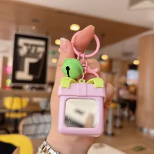 Detalle en primer plano del llavero de caja de regalo rosa con espejo pequeño y campana verde.