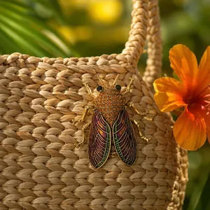 Close-up view of a vintage rhinestone cicada brooch pinned on a woven straw bag detail.
