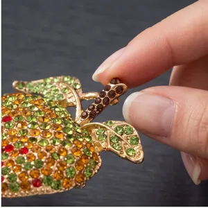 Close-up detail of the crystal apple brooch, sparkling gradient rhinestones and gold metal.