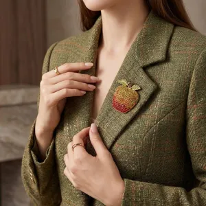 Close-up view of a stunning gradient rhinestone apple brooch on green tweed blazer detail.