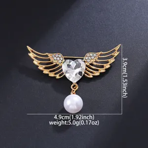 Gold angel wings brooch with sparkling crystal heart and pearl. Stylish fashion accessory.