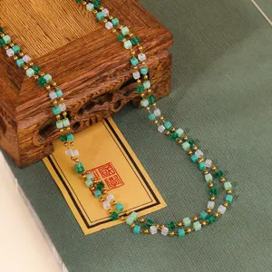 Close-up of green crystal square bead layered necklace with delicate gold chain detail.