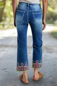 Detail view of women's denim jeans featuring intricate embroidered hem and slim fit straight cut.