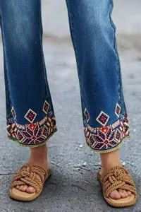 Detailed close-up shot of women's blue denim jeans featuring ethnic geometric embroidery cuffs.