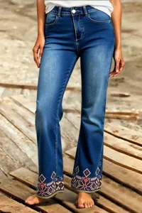 Detailed view of women's blue denim jeans featuring colorful geometric embroidery at cuffs.