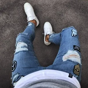 Detailed view of men's slim fit distressed denim jeans featuring cool patches and stylish rips.