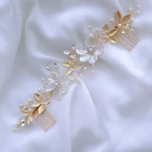 Dettaglio squisito di pettine per capelli da sposa dorato con fiori in resina bianca e perle.