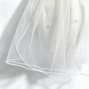 Close up detail of white bridal veil with pearl accents and delicate edge trim decoration.
