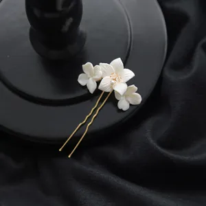 Vue rapprochée d'une épingle à cheveux fleur en céramique blanche artisanale avec tige dorée.