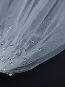 Close-up detail of bridal crystal rhinestone hair branch and delicate white tulle veil accessory.