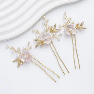 Primo piano di delicate forcine da sposa dorate con fiori rosa, perle e strass.