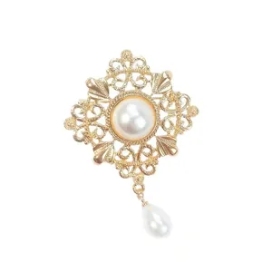 Vintage gold-tone brooch with central faux pearl and teardrop pendant, elegant accessory.