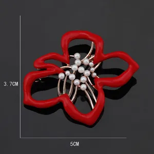 Detail shot of a red enamel flower brooch featuring pearl stamens and elegant metallic design.