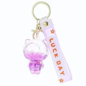 Kreativer Acryl Treibsand Bär Schlüsselanhänger mit lila Gurt und glitzernden Pailletten.