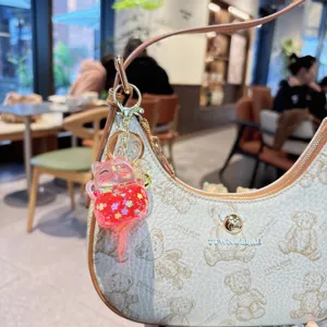Close-up detail of cream teddy bear print shoulder bag with liquid cat keychain charm.