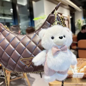 Cute fluffy teddy bear keychain with pink bow tie hanging on bag, soft plush toy pendant accessory.