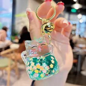 Clear oil-filled quicksand lucky cat keychain with green sequins and a gold bell pendant.