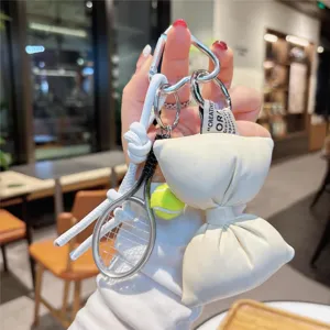 Closeup detail of white PU leather bow and tennis racket keychain handbag charm pendant accessory.
