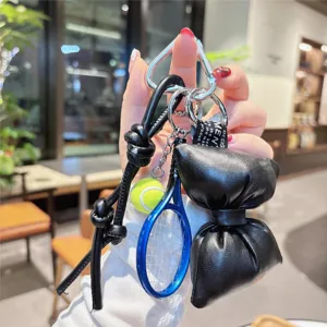Close-up detail of the black leather bow keychain with tennis racket charm and metal clip.