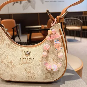Cute beige leather shoulder bag with bear print, metal logo, and a sweet pink beaded charm.