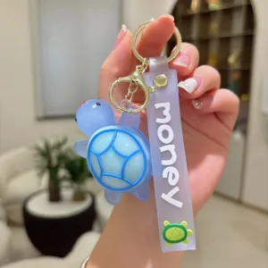 Detalle de llavero de tortuga azul, material de PVC suave con correa morada y anillo dorado.