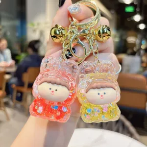 Close-up detail of the cute acrylic liquid glitter keychain with gold bell charms and cute cartoon design.