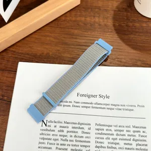 Primo piano del cinturino per orologio in nylon tessuto grigio con fibbia blu su sfondo in legno.