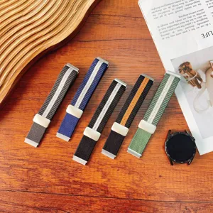Detailed view of striped nylon woven watch bands with magnetic folding buckles on a wooden desk.