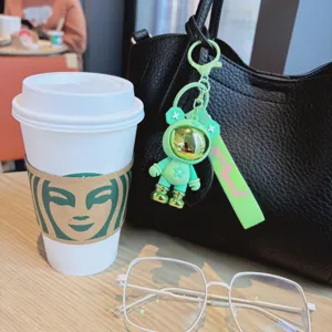 Primer plano del llavero de oso astronauta verde con correa Nice mood en bolso en cafetería.