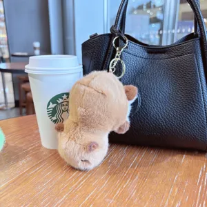 Detailed view of the cute plush capybara keychain hanging on a black handbag at a cafe.