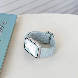 Detailed close-up of light mint braided watch band with silver watch case on minimalist white desk.
