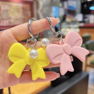 Close-up detail of cute acrylic bow keychain with pearl charm, colorful sweet style accessory.