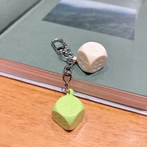 Close-up of a colorful macaron double dice metal keychain pendant resting on a book surface.