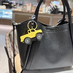 Nahaufnahme eines gelben Pick-up-Truck-Schlüsselanhängers an einer schwarzen Handtasche.