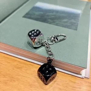 Close-up view of the double dice keychain with silver and black dice hanging on a book.