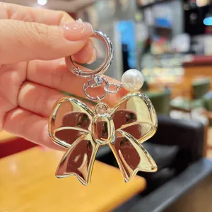 Detail view of a chic gold-tone metal bow keychain featuring an elegant white pearl pendant.