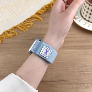 Blue nylon woven loop watch band compatible with Apple Watch, featuring a cute purple bow patch.