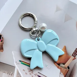 Close-up detail of light blue acrylic bow keychain with pearl and silver metal clasp decoration.