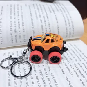 Miniature alloy monster truck keychain toy, detailed orange off-road car model on book background.