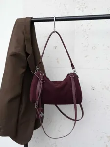 Detailed view of the burgundy suede shoulder bag hanging on a rack with hardware zipper and straps.