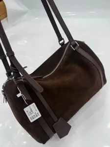 Close-up detail of the brown suede cylindrical shoulder bag, showing premium texture and strap.