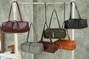 Minimalist cowhide boston bag detail showing multiple colors hanging on rack.
