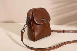 Detailed view of the brown leather crossbody phone bag with double zippers and metal button.