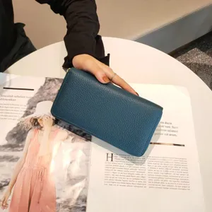 Detailed view of dark green genuine leather long wallet held over lifestyle magazine background.