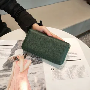 Dark green genuine leather long wallet detail shot, elegant pebble grain texture and zipper.