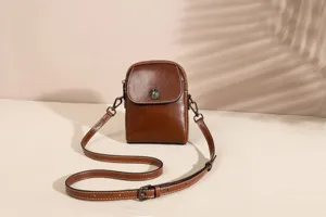 Detail view of brown leather crossbody phone bag with metal flower button and strap.